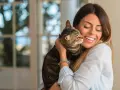Donna sorride abbracciando un gatto tigrato. Un momento di affetto che fa pensare a come educare un gatto con amore.