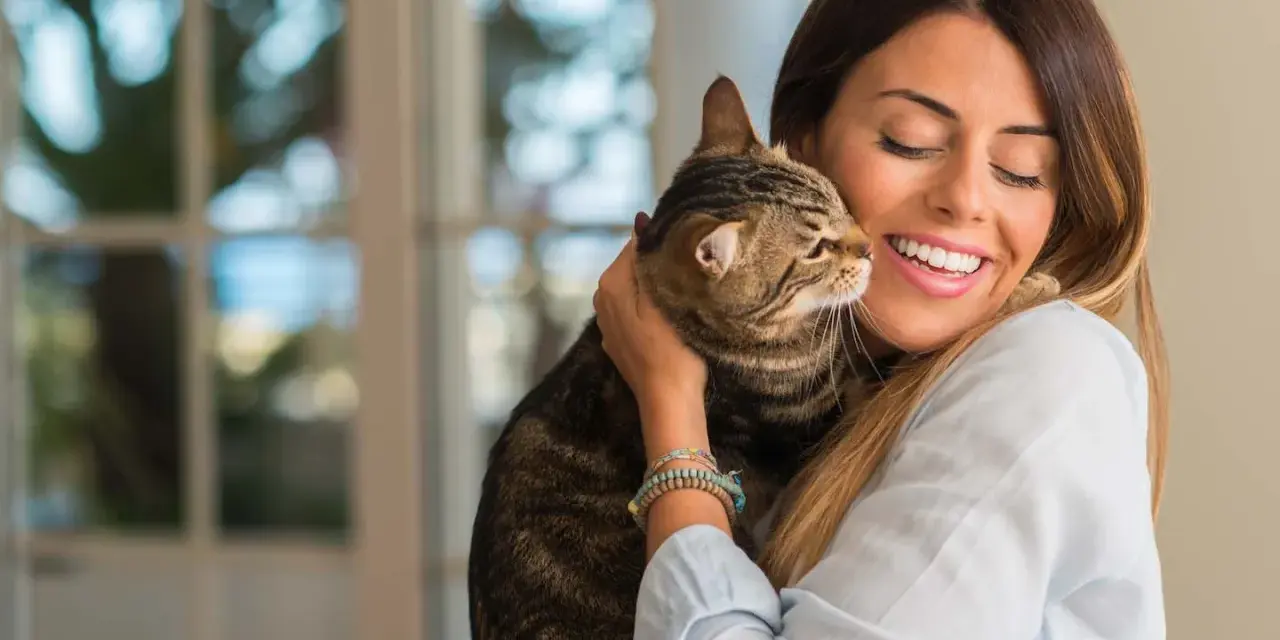 Donna sorride abbracciando un gatto tigrato. Un momento di affetto che fa pensare a come educare un gatto con amore.