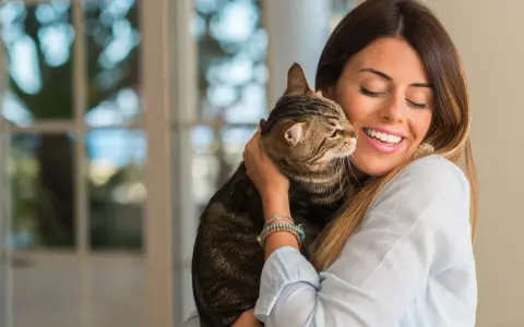 Donna sorride abbracciando un gatto tigrato. Un momento di affetto che fa pensare a come educare un gatto con amore.