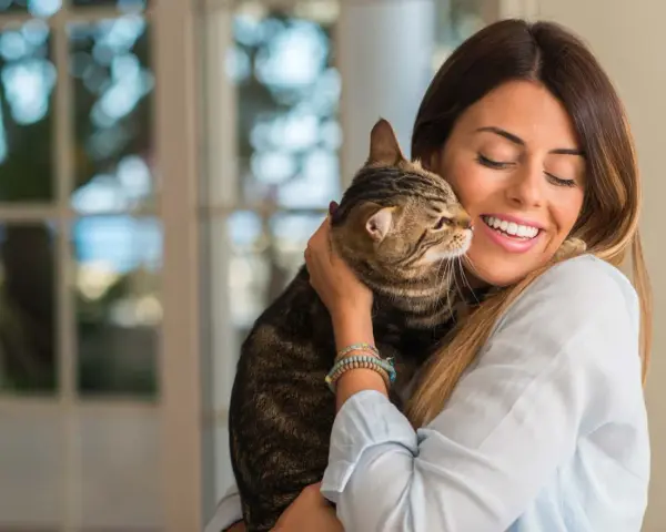 Donna sorride abbracciando un gatto tigrato. Un momento di affetto che fa pensare a come educare un gatto con amore.