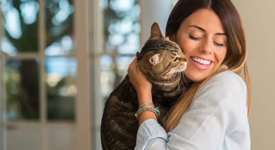 Donna sorride abbracciando un gatto tigrato. Un momento di affetto che fa pensare a come educare un gatto con amore.