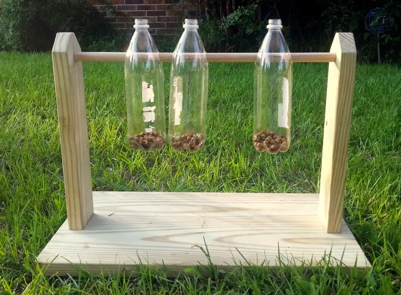 Gioco attivazione mentale cane fai da te: tre bottiglie di plastica con croccantini appese a un supporto in legno, pronte per stimolare il tuo amico a quattro zampe.